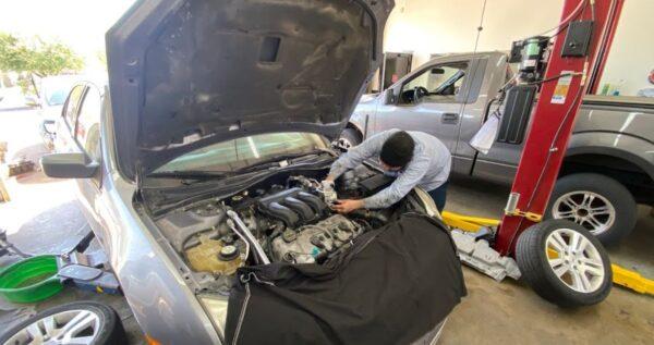 two cars in the bay with ones hood open and a technician working on the engine
